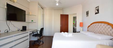 Habitación de hotel con cama, escritorio con computadora, silla, televisor montado en la pared y ventilador de techo.