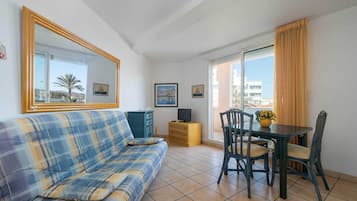A living room with a sofa, a table with chairs, a TV, and a window with curtains.