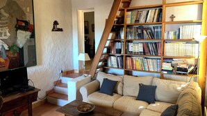 Uma sala de estar aconchegante com um sofá, uma mesa de centro, uma estante de livros e uma televisão.