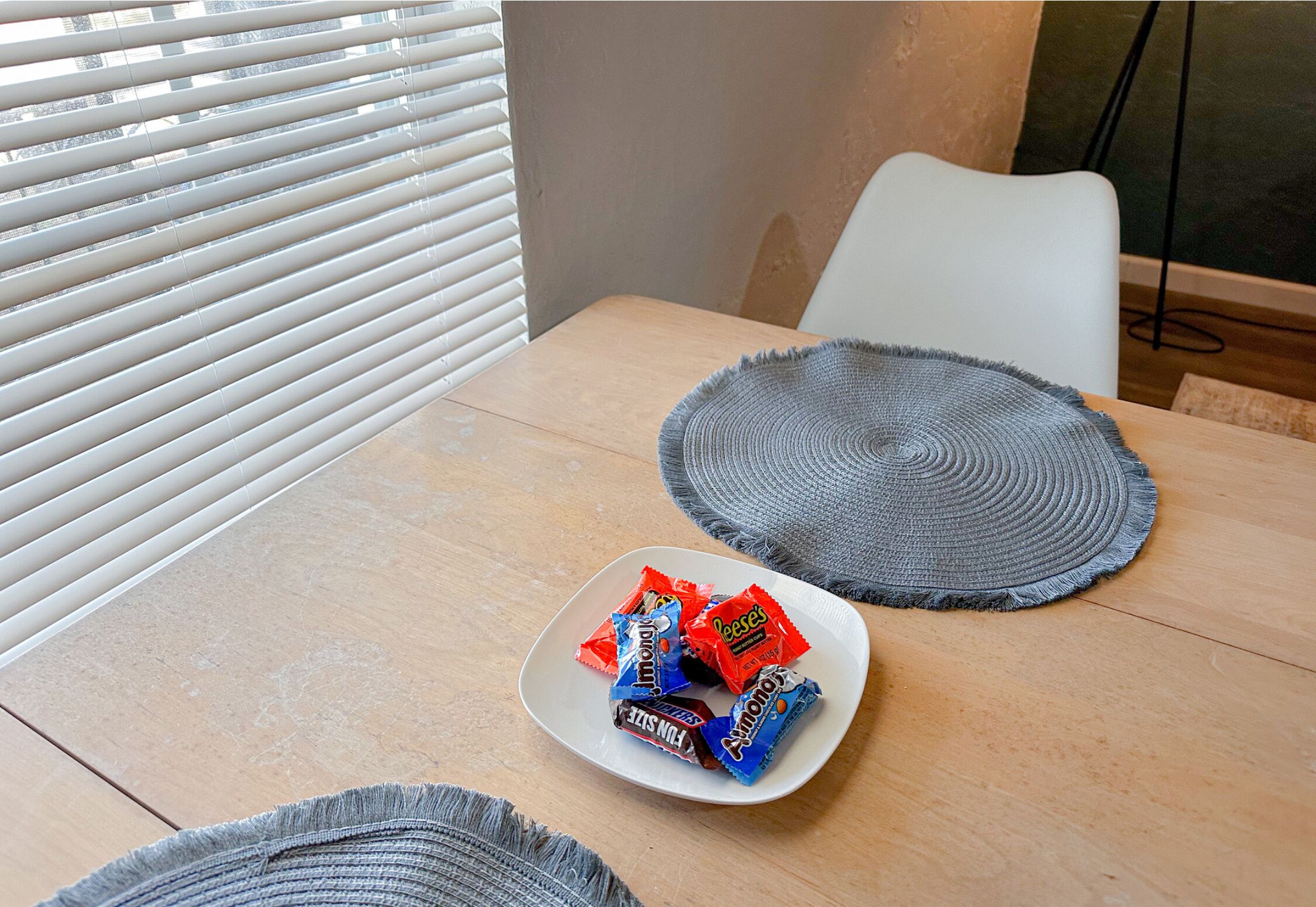 A dining table with a plate of candy, a woven placemat, and a chair.