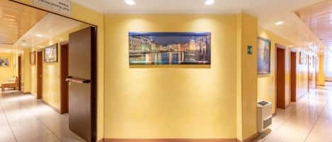 A hotel corridor with a painting of a cityscape, a sign indicating a video surveillance area, and a door leading to a room.