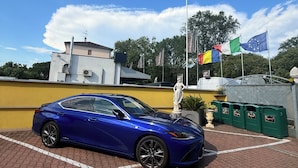 A blue car parked in a paved area with a statue and flags in the background. - Albergo Nuova Aurora  (Mestre)