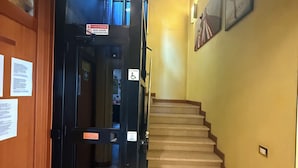 A staircase leading to an upper floor, a black elevator door, and a yellow wall with a framed picture. - Albergo Nuova Aurora  (Mestre)