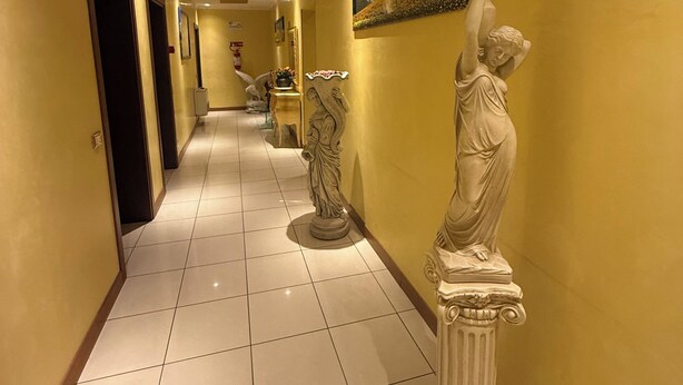 A hallway with a tiled floor, a statue, a framed picture, and a door. - Albergo Nuova Aurora  (Mestre)
