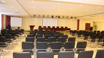 A conference room with rows of chairs, a podium, a screen, and a stage.