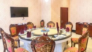 Ein runder Esstisch mit Stühlen, eine Chandelier, ein Fernseher an der Wand und eine Tür im Hintergrund.