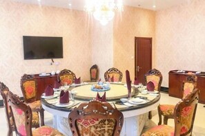 Ein runder Esstisch mit Stühlen, eine Chandelier, ein Fernseher an der Wand und eine Tür im Hintergrund.