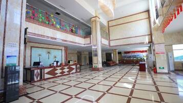 A spacious lobby with a checkered floor pattern, a reception desk, and a balcony with colorful decorations.