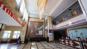 A spacious lobby with a high ceiling, a large chandelier, a checkered floor, and a mural on the wall.