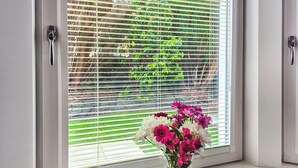 A window with blinds, a vase with flowers, and a view of greenery outside. - 1 bedroom accommodation in Dunoon (Dunoon)