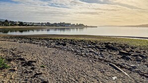A riverside view with a rocky shoreline, calm water, and a distant town with buildings. - 1 bedroom accommodation in Dunoon (Dunoon)