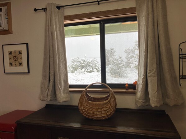 A wicker basket on a wooden dresser by a window with white curtains.