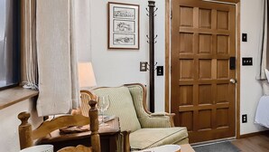 A cozy room with a wooden door, a green upholstered chair, a wooden table with a glass, and a patterned rug.