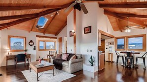 A spacious loft with high ceilings, wooden beams, and large windows offering views of the outdoors.