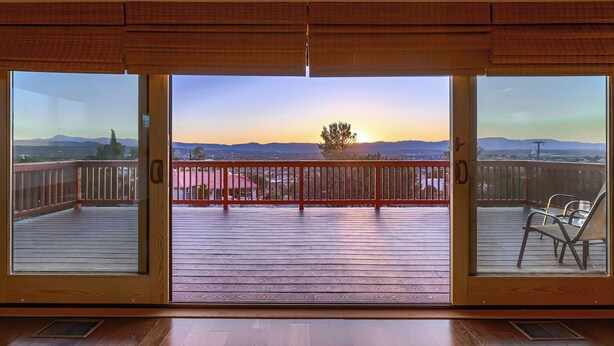 A room with a view of a sunset over a cityscape, a wooden deck, and a red railing.