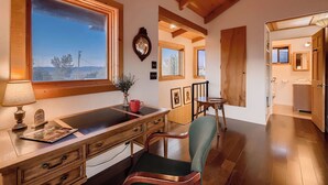A room with a wooden desk, a chair, a window with a view, and a door leading to a bathroom.