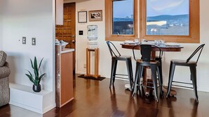 A dining area with a wooden table and four chairs, a water dispenser, and a view of the sea through large windows.