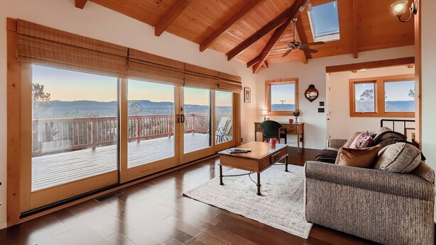 A spacious living room with a wooden ceiling, large sliding glass doors leading to a deck, a cozy sofa, and a small desk with a chair.