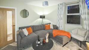 Ein Wohnzimmer mit grauem Sofa, einem weißen Sessel, einem schwarzen Couchtisch und einem gemusterten Teppich.