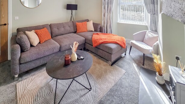 Ein modernes Wohnzimmer mit einem Ecksofa, einem runden Couchtisch und einem weißen Sessel.
