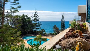 A pool with a view of the ocean, surrounded by tropical plants and rocks. - Solar do Mar by LovelyStay (Funchal)
