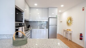 A modern kitchen with white cabinets, a stainless steel refrigerator, a granite countertop, and a small wooden table with a mirror. - Solar do Mar by LovelyStay (Funchal)