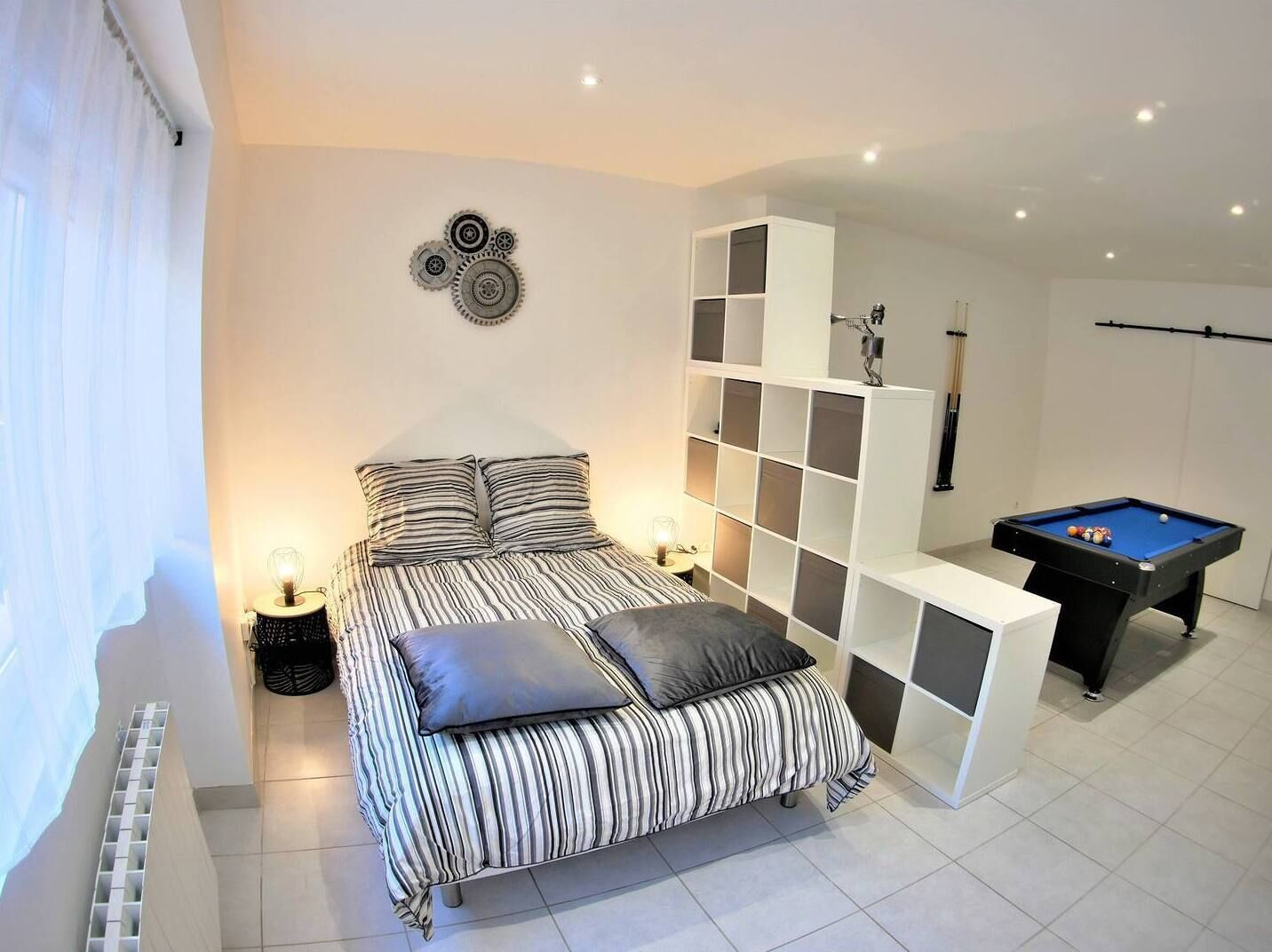 A bedroom with a striped bed, a pool table, and a white shelving unit.