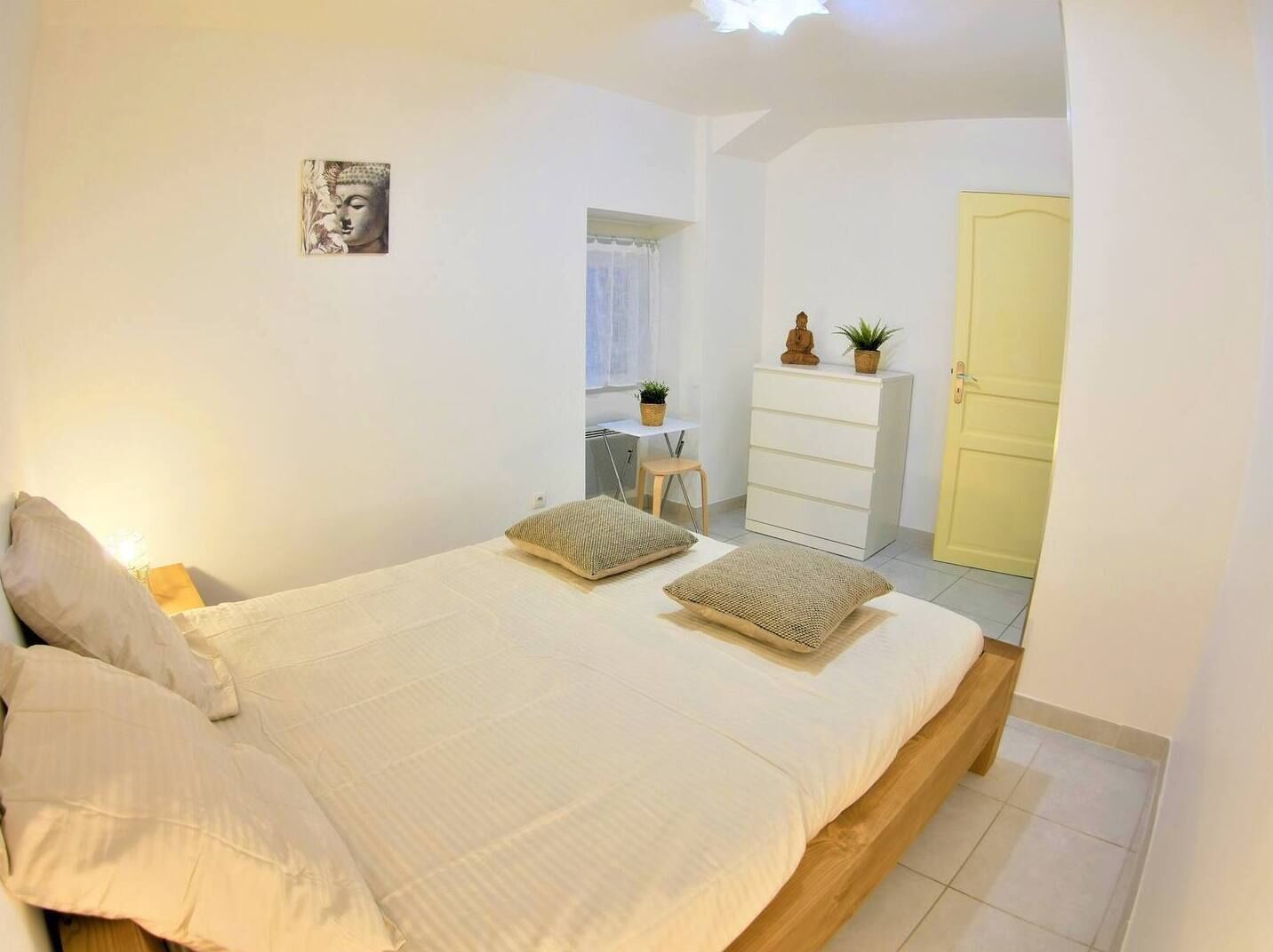 A bedroom with a bed, pillows, a desk, a chair, a wardrobe, and a door.