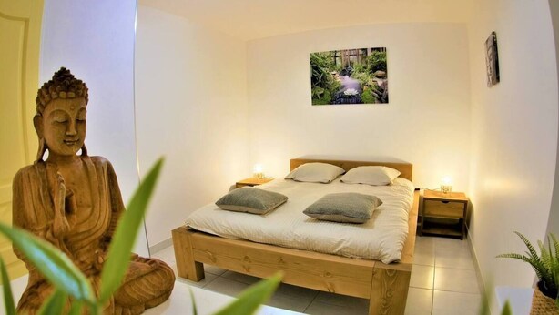 Ein Schlafzimmer mit einem hölzernen Bett, zwei Nachttischen, einem Wandbild und einer Buddha-Statue.