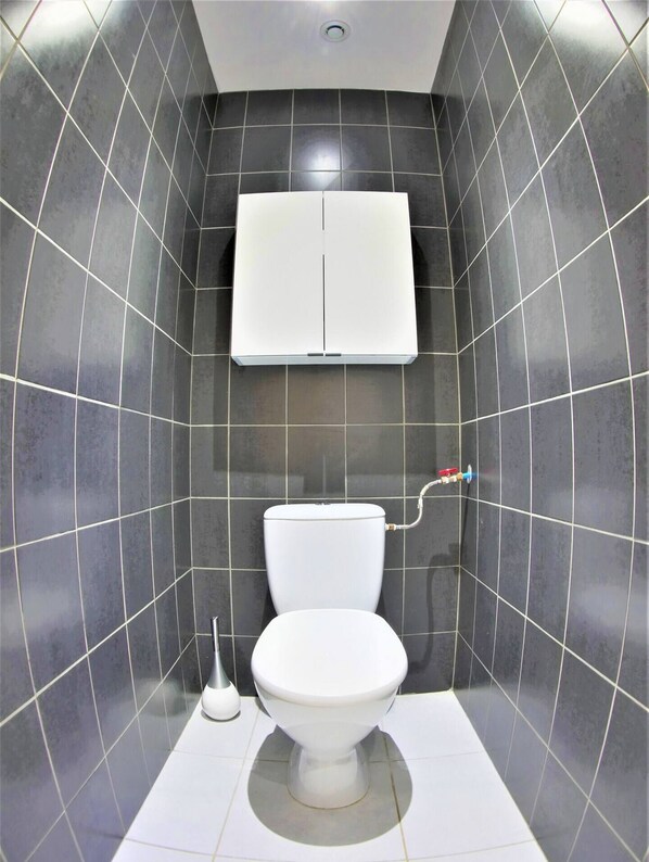 A bathroom with a white toilet, a wall-mounted toilet paper holder, and a white cabinet above the toilet. - Le Salséro - Large, cozy *** apartment for 8 people, with parking included, (Nîmes)