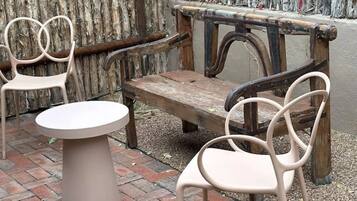A patio area with a round table and two chairs, a wooden bench, and a rustic wooden fence in the background.