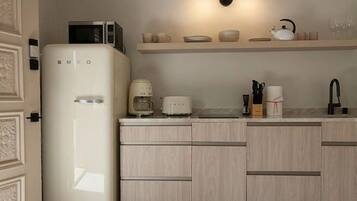 A compact kitchen with a white refrigerator, a microwave, a coffee maker, a toaster, and a sink.