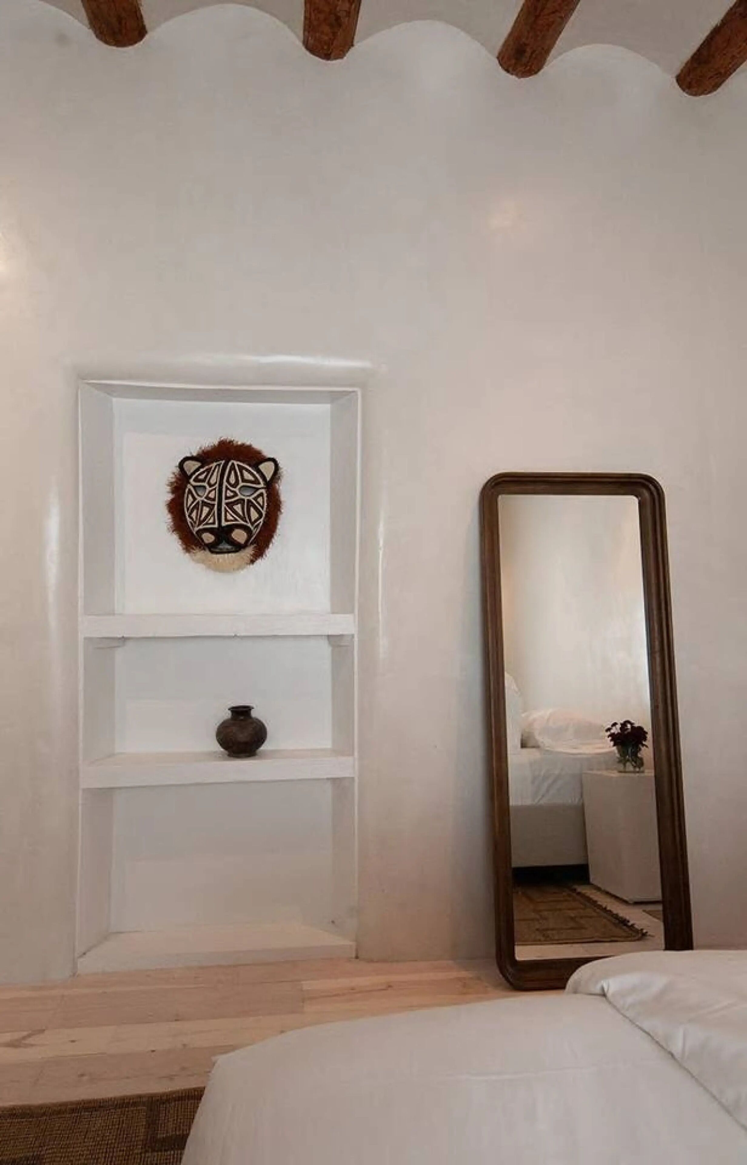 A bedroom with a bed, a mirror, and a wall-mounted shelf with decorative items.