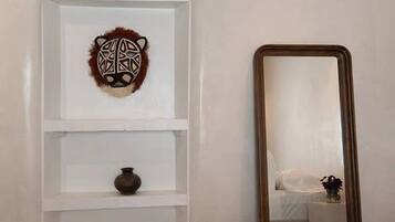 A bedroom with a bed, a mirror, and a wall-mounted shelf with decorative items.