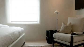 A bedroom with a large window, a bed, a chair, and a floor lamp.