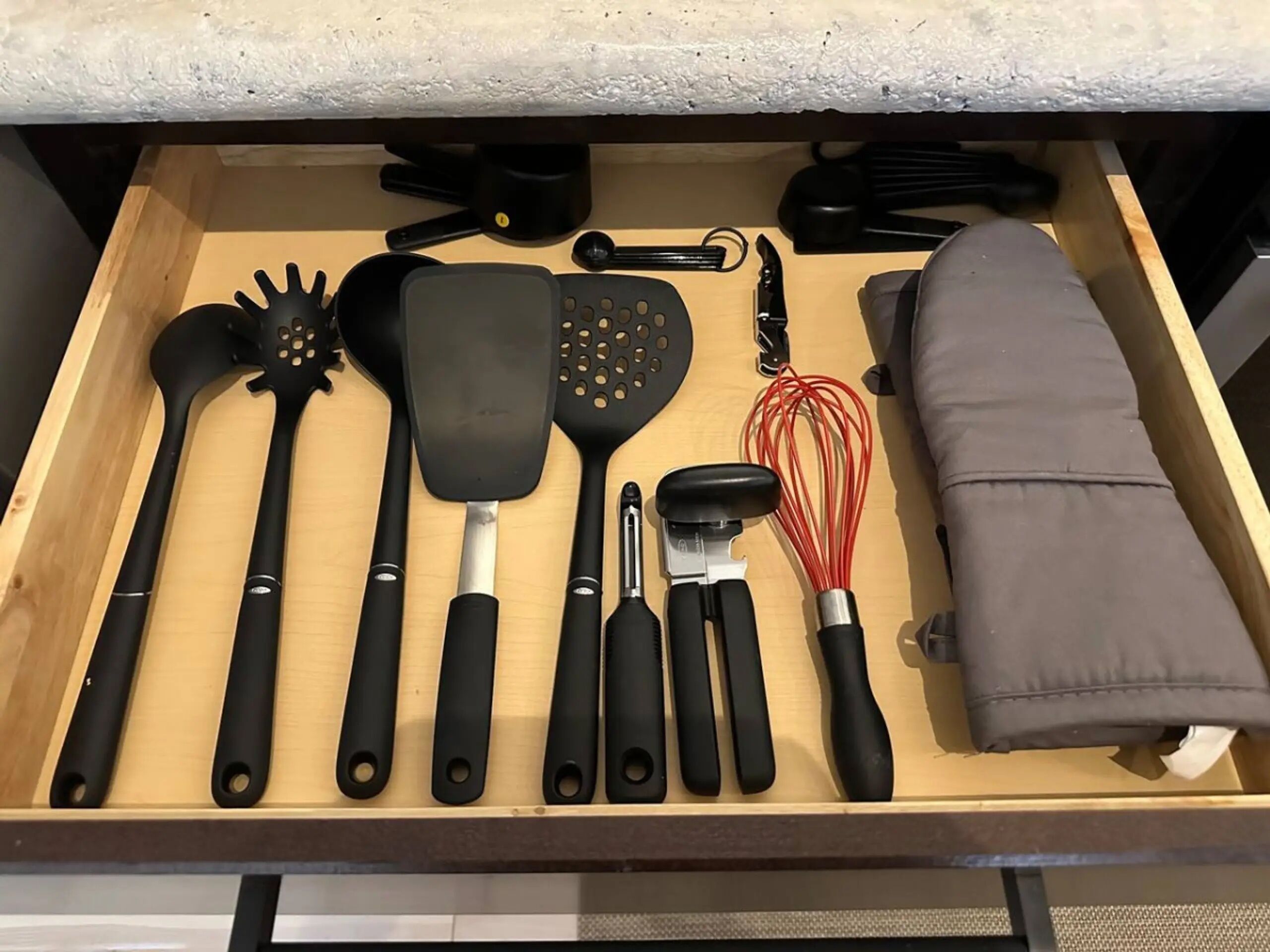 A drawer containing various kitchen utensils including spatulas, a whisk, and a grater.
