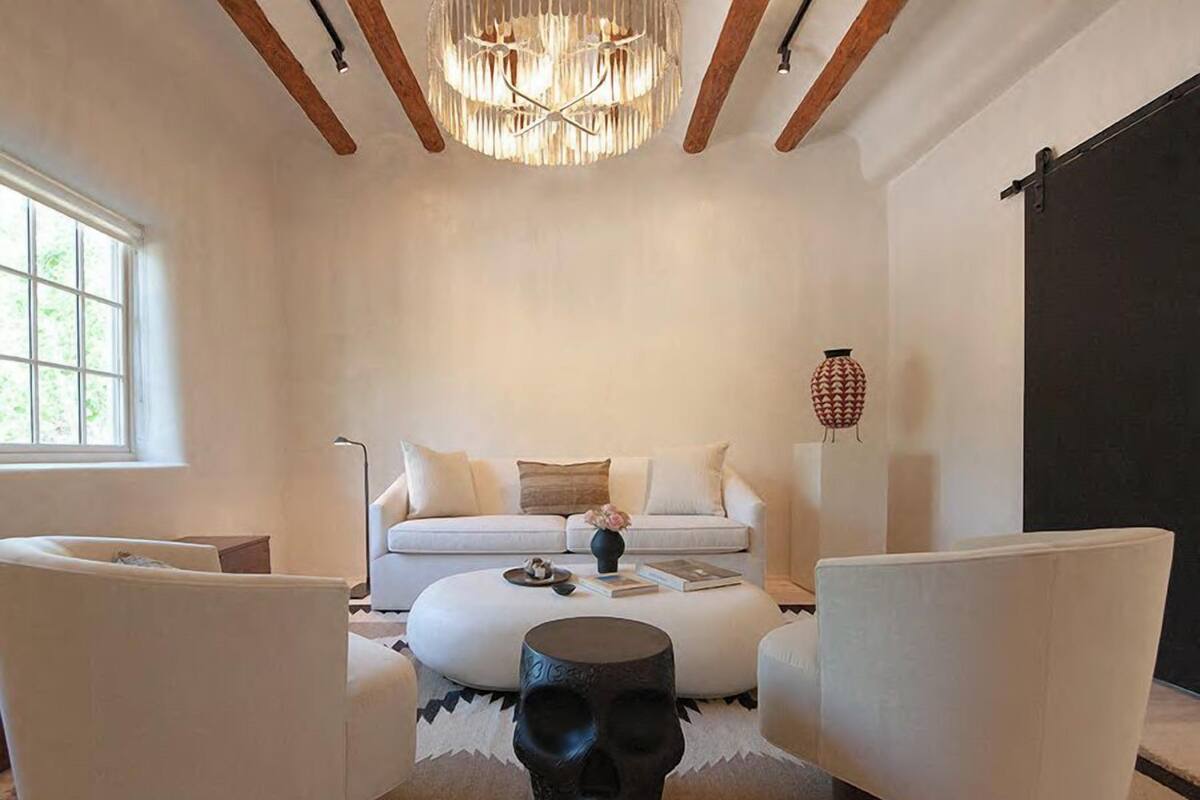 Una sala de estar moderna con un sofá blanco, dos sillones blancos, una mesa de centro redonda y una escultura negra original.