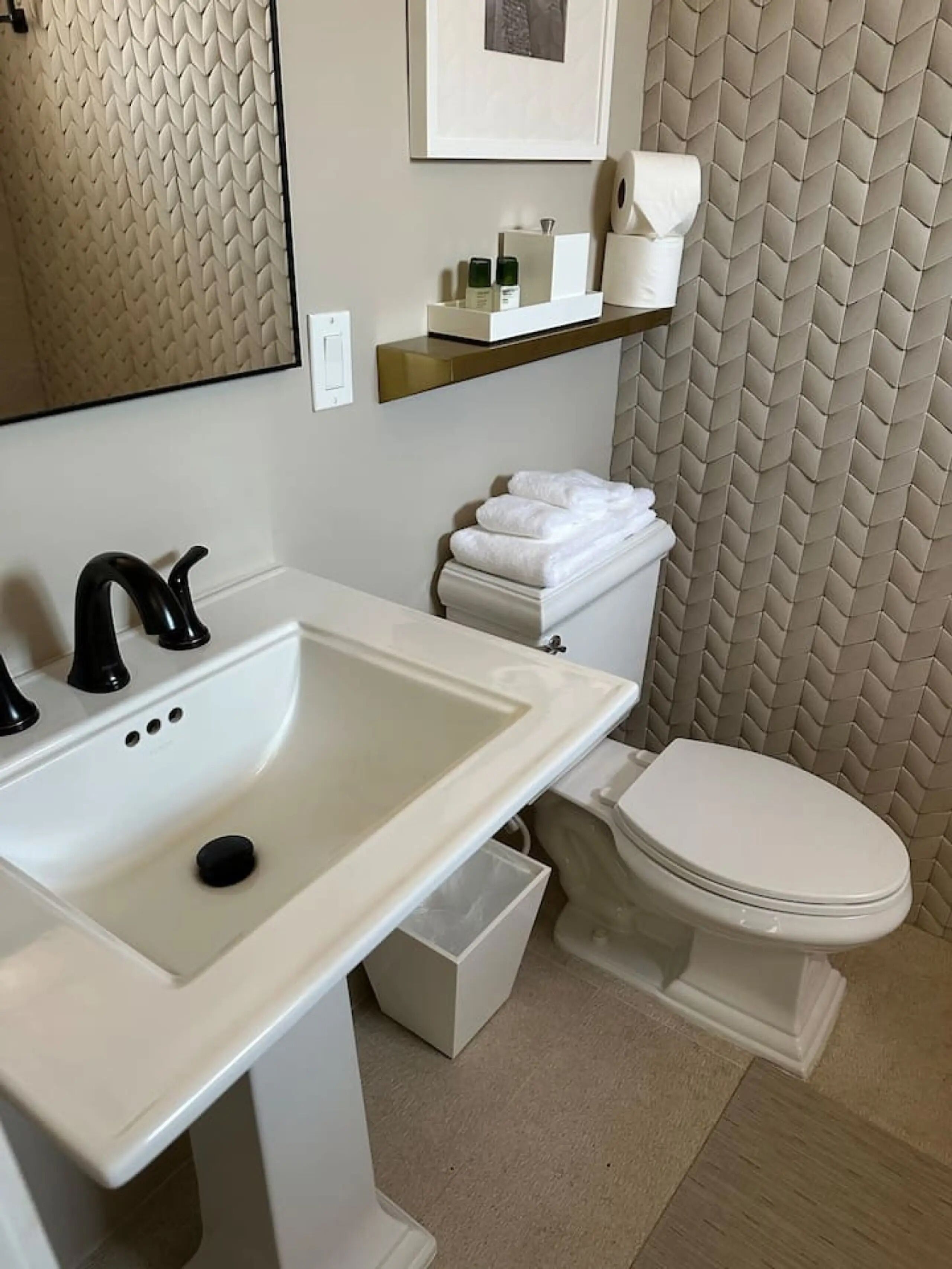 A bathroom with a white sink, black faucet, white toilet, and beige textured wall.