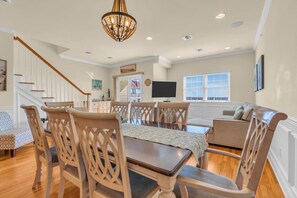 A spacious dining area with a wooden table and chairs, a staircase, and a large window with a view.
