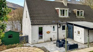 Una casa con fachada de piedra, techo de tejas oscuras y un pequeño porche con mobiliario exterior.
