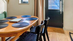 Un comedor con una mesa de madera, sillas negras y individuales azules. Hay dos ventanas y una puerta con vistas a árboles.