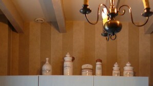 Une cuisine avec des meubles blancs, un évier et une cuisinière. On peut voir des bocaux sur les meubles hauts et un lustre au-dessus.