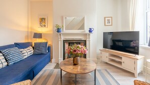 Una sala de estar con un sofá azul, una chimenea, un televisor y una mesa de centro con flores.