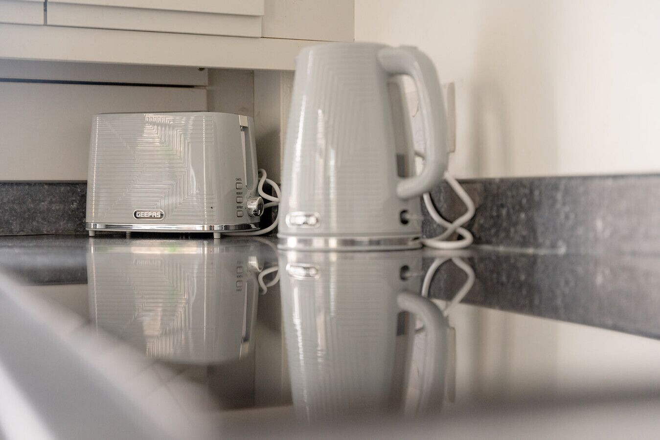 Una cocina con cafetera GEERAS y una taza blanca sobre una encimera reflectante.