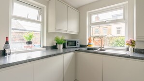 Cocina con alacenas blancas, encimera de granito, microondas, lavamanos y dos ventanas.