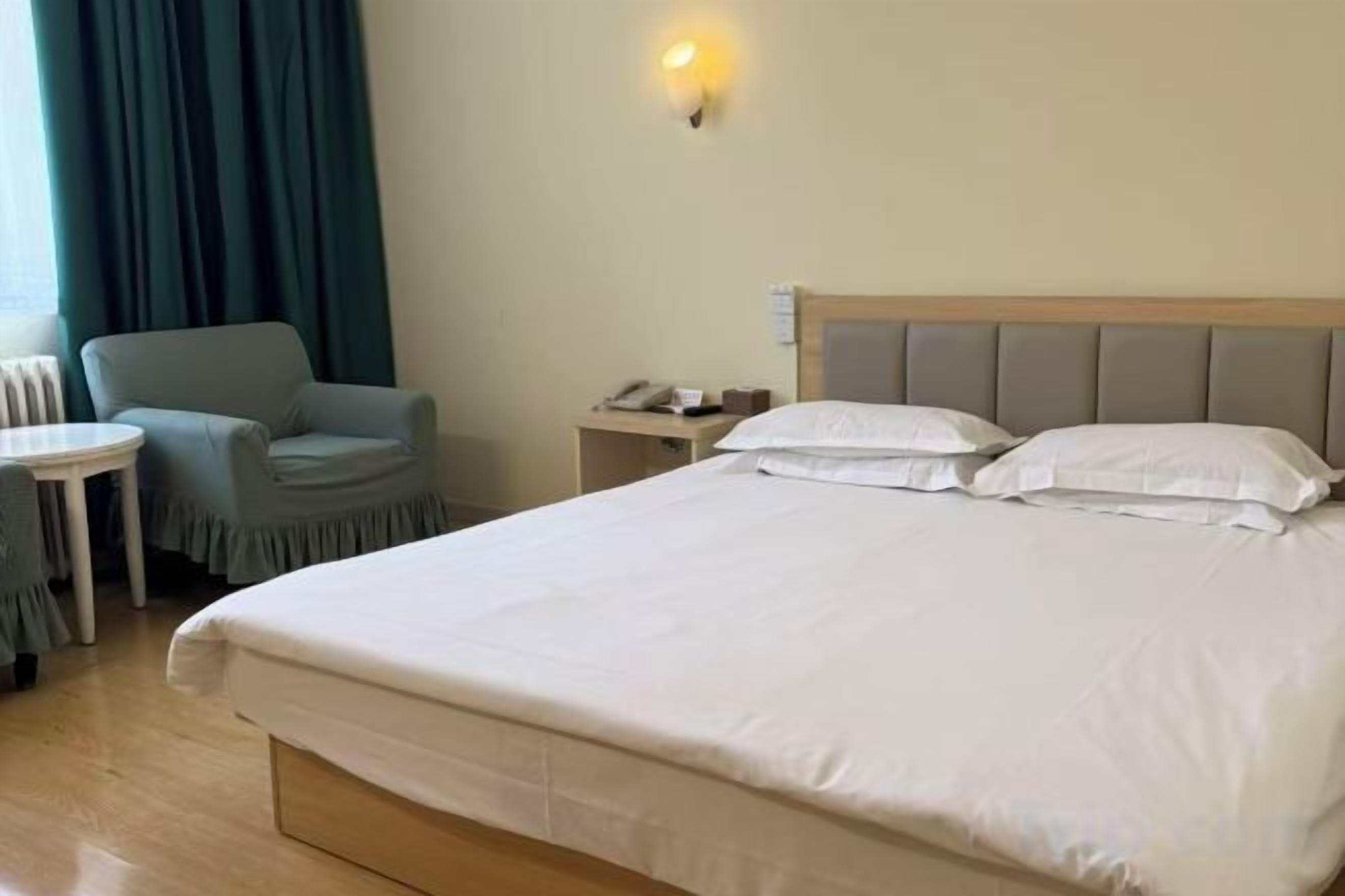 A hotel room with a bed, a chair, a small table, and a nightstand with a lamp.