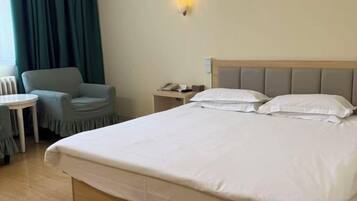 A hotel room with a bed, a chair, a small table, and a nightstand with a lamp.