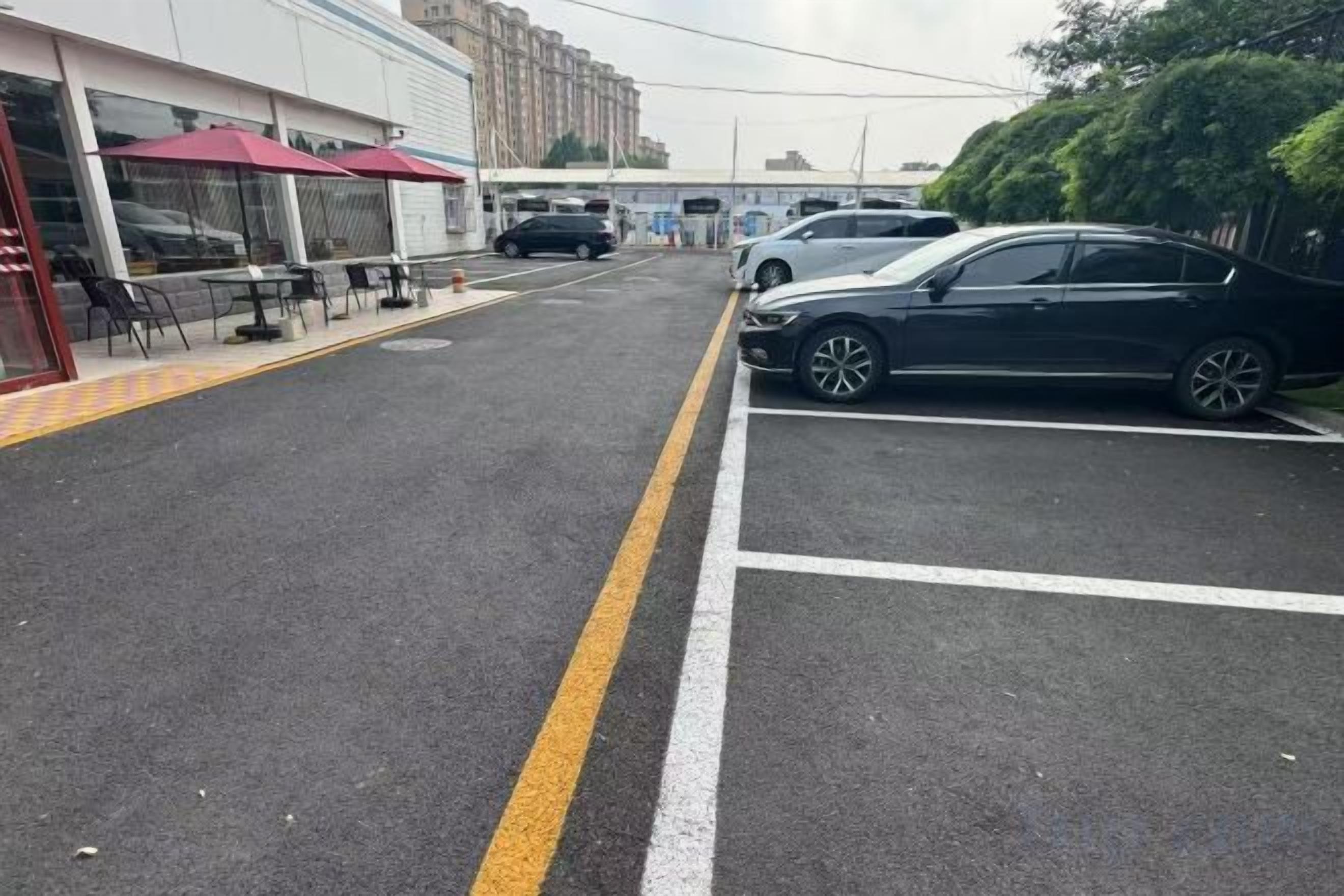 Un parking rempli de voitures, un bâtiment doté d’une terrasse, et un ciel dégagé.