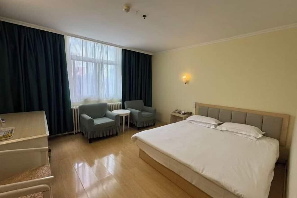 A hotel room with a bed, a desk, two chairs, a small table, and a window with curtains.