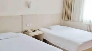 A hotel room with two beds, a bedside table with a phone, and a window with curtains.